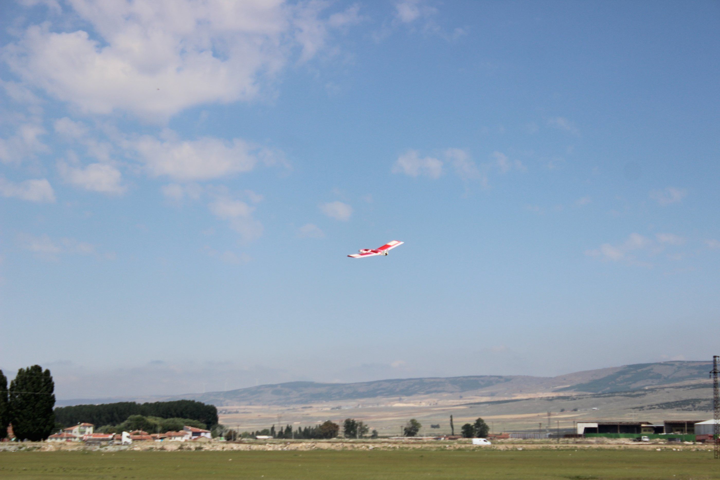 A red-and-white UAV in flight over open country